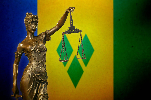 Close-up van een bronzen beeldje van Lady Justice voor een vlag van Saint Vincent en de Grenadines. - Foto, afbeelding