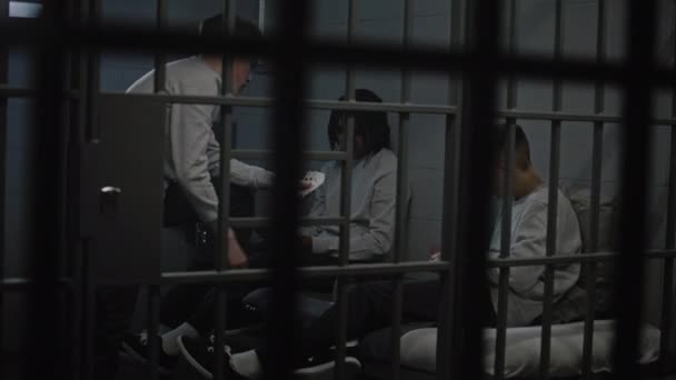 Tre prigionieri adolescenti multietnici giocano a carte in cella. I giovani criminali scontano una pena detentiva per crimini in prigione. Centro di detenzione minorile o penitenziario. Vista attraverso barre metalliche. - Filmati, video