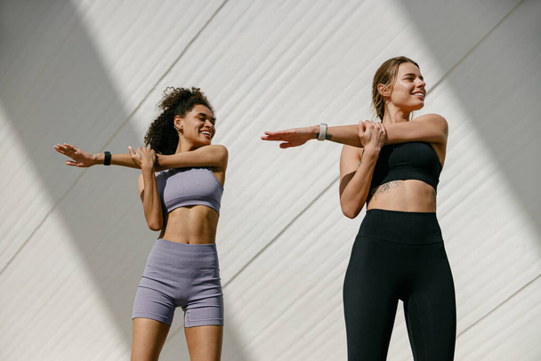 Eşofmanlı genç sporcu kadınlar dışarıda esniyorlar ve koşuya hazırlanıyorlar. Sağlıklı yaşam konsepti - Fotoğraf, Görsel