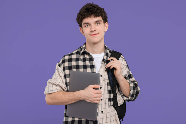 Portrait of student with backpack and laptop on purple background - Φωτογραφία, εικόνα