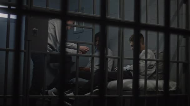Multicultural young criminals play card games in prison cell. Teenage prisoners serve imprisonment term for crimes in jail. Youth detention center or correctional facility. View through metal bars. - Footage, Video