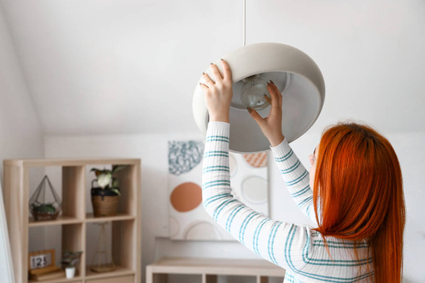 Mujer bastante joven que cambia la bombilla en la lámpara en casa - Foto, imagen