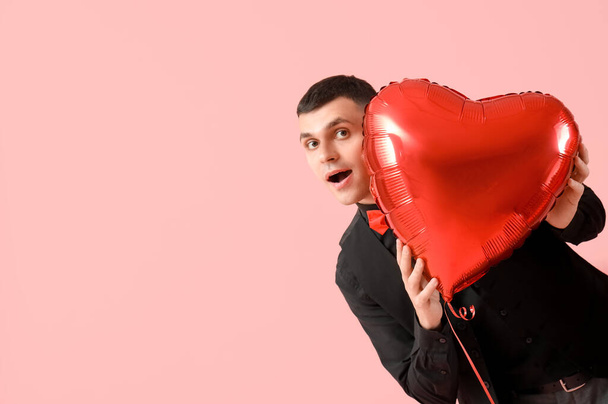 Sorpreso giovane uomo con palloncino d'aria a forma di cuore per San Valentino su sfondo rosa - Foto, immagini