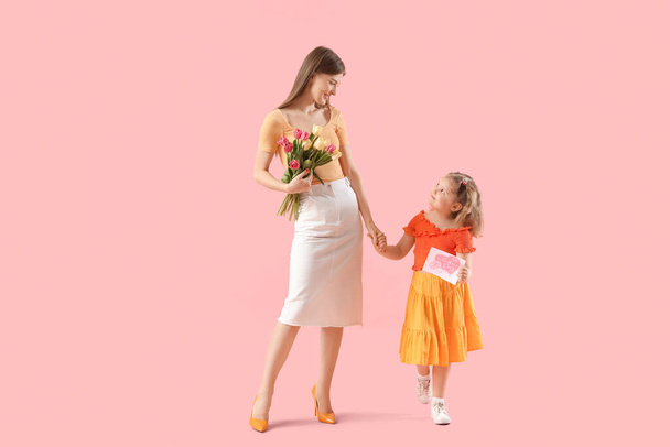 Klein meisje en haar moeder met boeket van tulpen en wenskaart op roze achtergrond. Moederdag viering - Foto, afbeelding