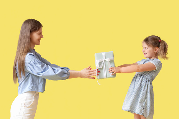 Kleines Mädchen begrüßt seine Mutter mit Muttertag mit Geschenkbox auf gelbem Hintergrund - Foto, Bild