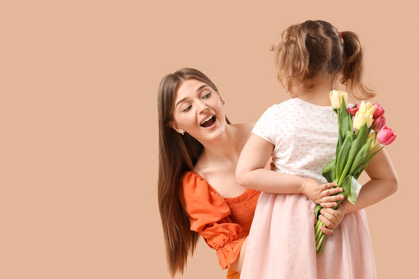 Petite fille cachant bouquet de tulipes pour maman derrière son dos sur fond beige. Concept de la fête des mères - Photo, image