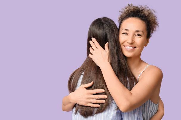 Beautiful mature woman hugging her teenage daughter on lilac background. Mother's day - Photo, Image