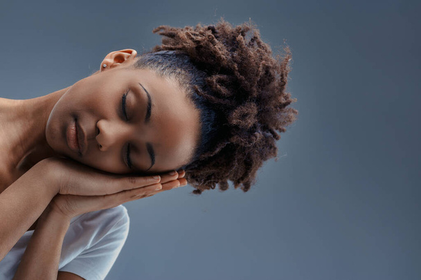 Mírumilovná mladá žena odpočívající hlavou na rukou, oči zavřené v poklidném odpočinku na šedém pozadí - Fotografie, Obrázek