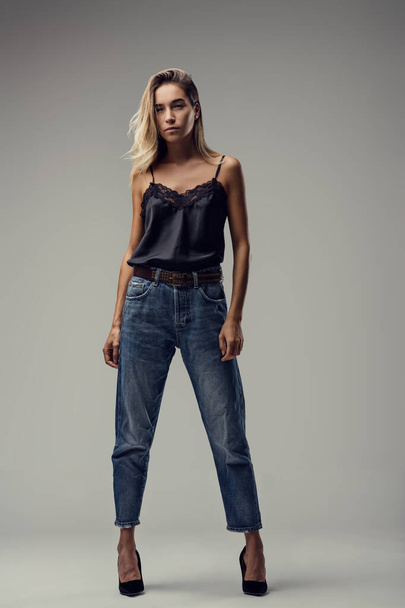 Eleganz in Schlichtheit, das Bild zeigt sie in einem schwarzen Top aus Spitze, Jeans und High Heels, die lässige Anmut verströmen - Foto, Bild