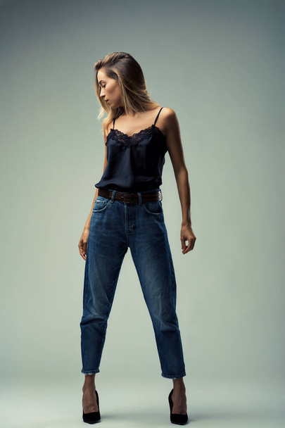 Полный портрет молодой женщины, сочетающей случайные джинсы с тонкой женственностью кружевного черного топа - Фото, изображение