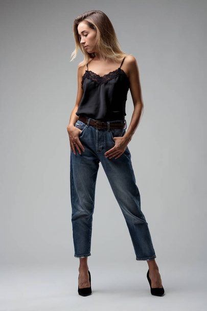 Женщина стоит с расслабленной, но напористой осанкой, ее черный кружевной топ и прочные джинсы джинсы джинсы проекции усилий шик - Фото, изображение