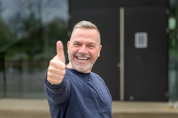Заманчиво мотивированный привлекательный мужчина средних лет показывает большим пальцем вверх жест одобрения и успеха с мрачной улыбкой
 - Фото, изображение