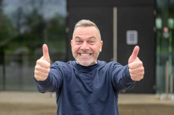 Мотивированный привлекательный мужчина средних лет с удвоенной улыбкой поднимает вверх большие пальцы в знак одобрения и успеха - Фото, изображение