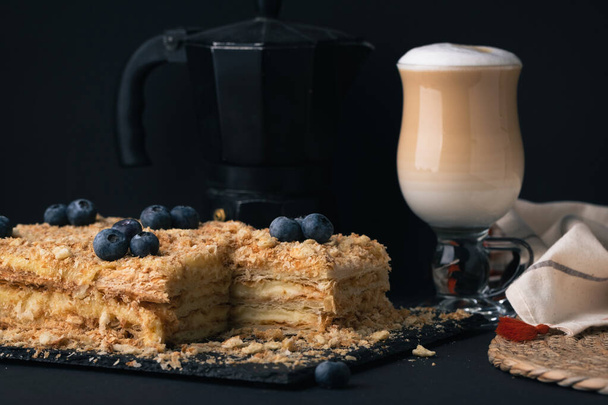Mézes torta egy pohár latte kávé mellett. Cappuccino kávé házi süteményt a fekete háttér. - Fotó, kép