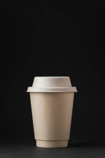 Blank paper cup of hot coffee with paper lid on the black background. Mock up with copy space for a free text - Photo, Image