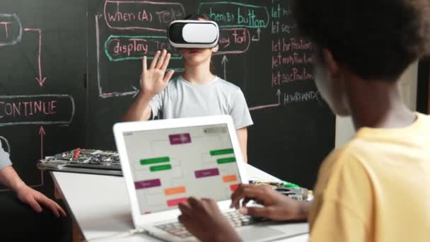 African boy programming system while caucasian girl enter metaverse while sitting at blackboard with engineering code written.high school girl wearing VR or headset in STEM technology. Edification - Footage, Video
