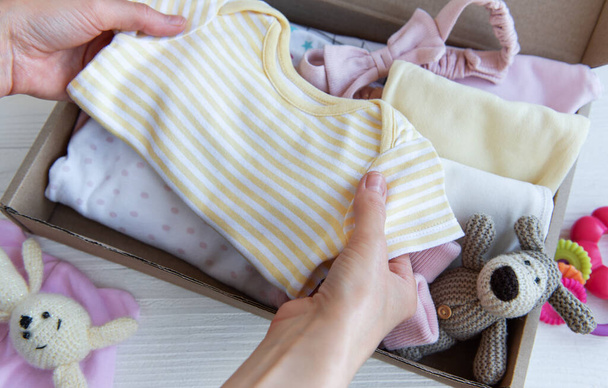 Τα χέρια των γυναικών συλλέγουν παιδικά ρούχα σε κουτιά. Η έννοια της προετοιμασίας για τη γέννηση ενός παιδιού ή μιας δωρεάς. - Φωτογραφία, εικόνα