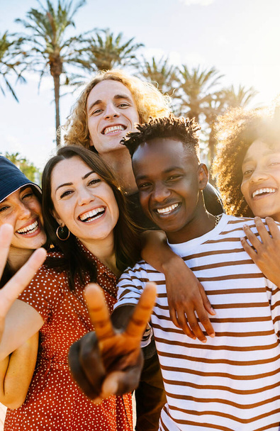 Vertikale Porträtgruppe junger multikultureller trendiger Freunde, die vor dem Hintergrund von Palmen in die Kamera schauen. Outdoor-Foto von verschiedenen glücklichen Menschen, die Spaß im Sommer haben. - Foto, Bild