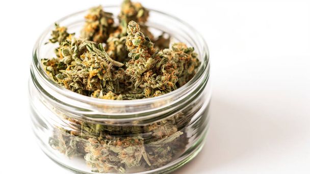 Droge cannabisknoppen in een glazen pot tegen een witte achtergrond. - Foto, afbeelding