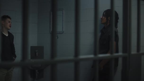 Group of teen prisoners talk with each other in jail cell. Multi ethnic teenagers serve imprisonment term in detention center. Young inmates in prison cell. Justice system. View through metal bars. - Footage, Video