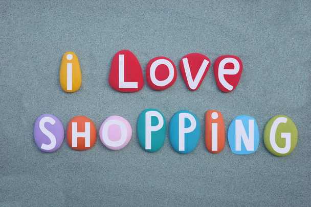Me encanta ir de compras, lema creativo compuesto con letras de piedra multicolor pintadas a mano sobre arena verde - Foto, imagen