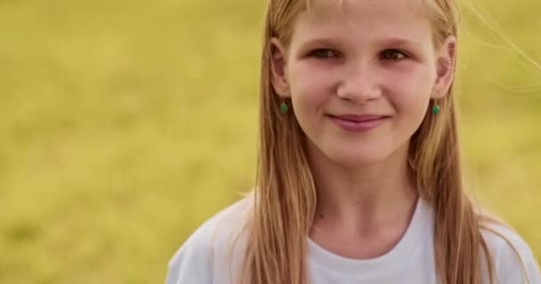 Close-up portret van jong blond meisje draaien haar hoofd, kijken naar de camera en naar de hemel. Niet-stedelijke scene, winderige dag, geel veld, openhartig lachend kind, Oekraïense tiener. Hoge kwaliteit 4k beeldmateriaal - Video
