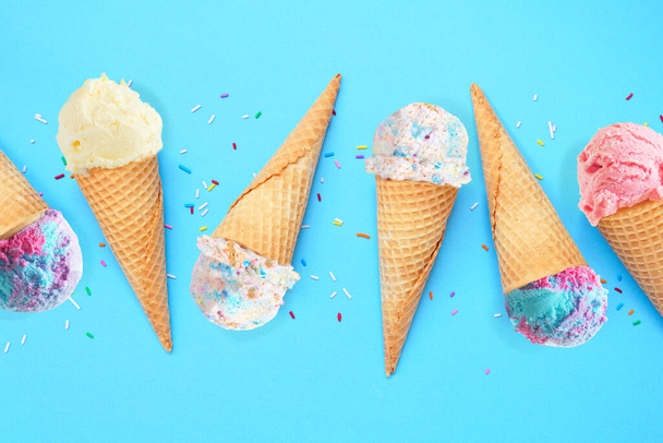 Літній конус морозива лежав на синьому фоні. Різноманітність пастельних кольорових смаків. - Фото, зображення