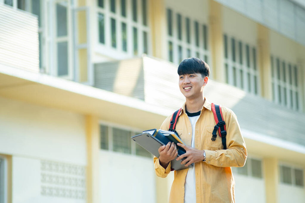 Un estudiante universitario satisfecho llevando una computadora portátil y libros camina por los terrenos del campus, exudando una sensación de preparación y entusiasmo por el aprendizaje. - Foto, imagen