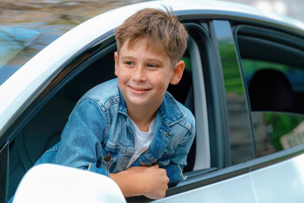 Podekscytowany i szczęśliwy młody chłopiec z uśmiechem na twarzy pojawia się na oknie samochodu podczas jazdy, zabawny i wesoły wyraz twarzy podczas podróży samochodem w okresie letnim. Wieczne - Zdjęcie, obraz