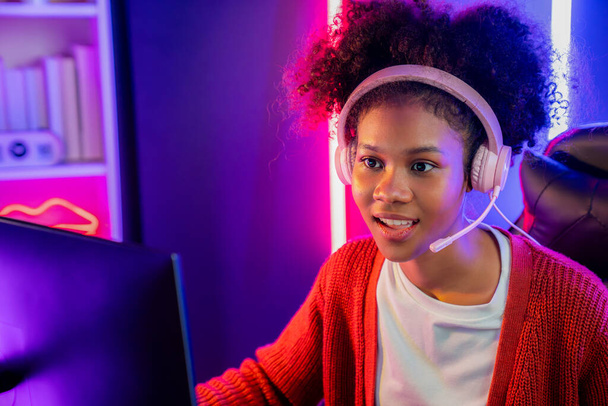 Afro-Amerikaanse meisje streamer spelen online vechten met Esport ervaren team het dragen van een koptelefoon in neon kleur verlichting kamer. Praten met andere spelers planing strategieën om concurrenten te winnen. Smaakstof. - Foto, afbeelding