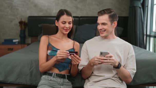 Junges Paar sitzt mit Online-Bezahlapp und digitalem Portemonnaie am Smartphone im heimischen Schlafzimmer, um mit Kreditkarte zu bezahlen. E-Commerce-Einkauf und moderner Einkauf über das mobile Internet. Stollen - Filmmaterial, Video