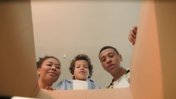 Открывающаяся внутри картонная коробка радостно удивляет веселую африканскую семью родителей сына маленького мальчика малыша, заказывающих доставку расфасованной посылки интернет-магазина в день переезда - Кадры, видео