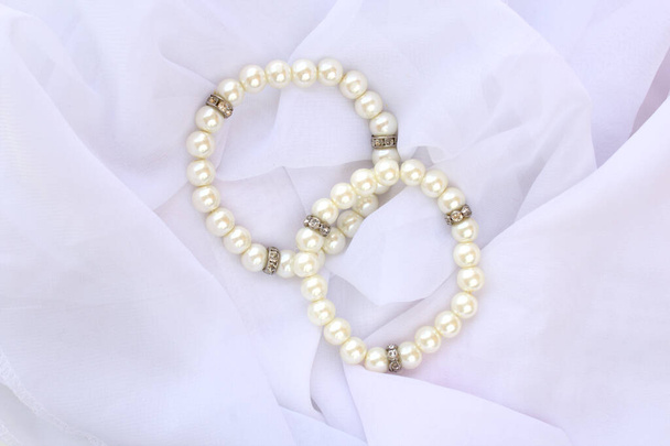 Dos brazaletes de perlas falsas de marfil para llevar de novia. Joyería de moda femenina en la parte superior de tela de velo blanco. - Foto, Imagen