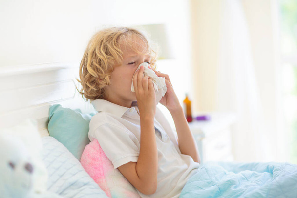 Sick child in bed. Mother checking on unwell kid. Little boy having fever feeling ill. Mom with thermometer and cough medicine. Young patient coughing and sneezing. Flu prevention and treatment. - Photo, Image