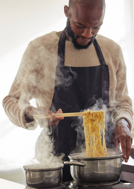 Man, cooking noodles and pot with steam at home for lunch or dinner, busy and hungry for food with preparation. Catering, African chef with chopsticks for Asian cuisine and nutrition in kitchen. - Photo, Image