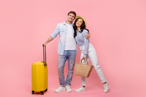 Vue complète du corps de l'homme et de la femme se préparant pour le voyage avec valise, posant et embrassant isolé sur fond rose - Photo, image