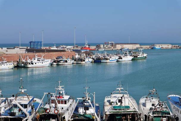 Termoli, Molise, Italië 12 april 2024: De haven van Termoli, dicht bij de Borgo Antico, gekenmerkt door een pier voor vissersboten en de Guardia di Finanza, een tussenpier voor het instappen voor de Tremiti-eilanden, en de pier op de werf in het noorden - Foto, afbeelding