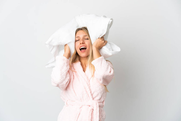 Giovane donna bionda isolata su sfondo bianco in pigiama e con in mano un cuscino stressato sopraffatto - Foto, immagini