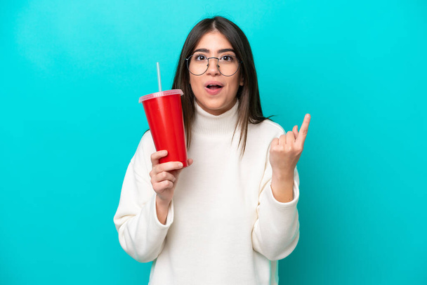 Young caucasian woman drinking soda isolated on blue background intending to realizes the solution while lifting a finger up - Foto, imagen
