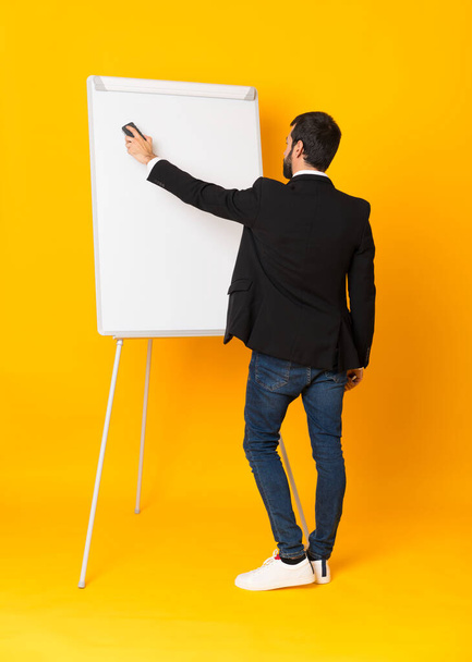 Full-length shot of businessman giving a presentation on white board over isolated yellow background - Photo, Image