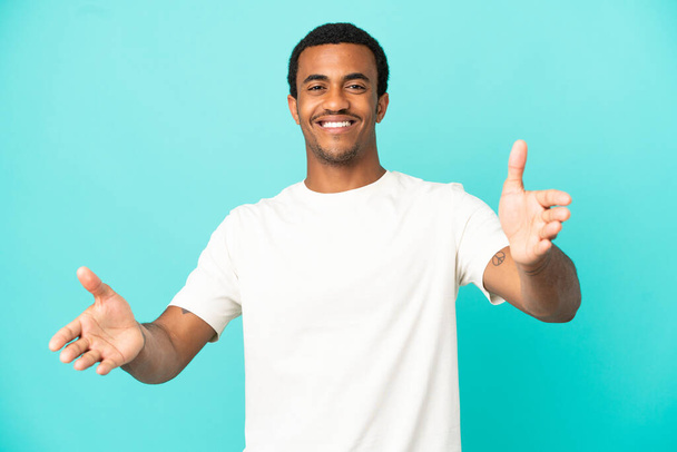 Afroamerikanisch aussehender Mann auf isoliertem blauem Hintergrund, der präsentiert und einlädt, mit der Hand zu kommen - Foto, Bild