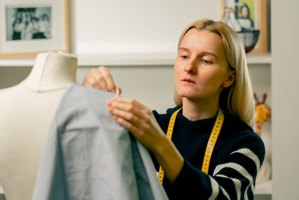 en un taller de costura costurera trabaja con un maniquí y alfileres de tela azul con un alfiler - Foto, Imagen