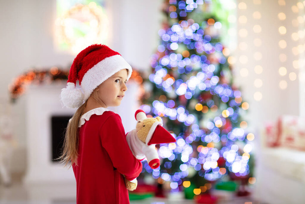 Οικογένεια το πρωί των Χριστουγέννων στο τζάκι. Παιδιά που ανοίγουν χριστουγεννιάτικα δώρα. Παιδιά κάτω από το χριστουγεννιάτικο δέντρο με κουτιά δώρων. Διακοσμημένο σαλόνι με παραδοσιακό τζάκι. Ζεστή ζεστή χειμωνιάτικη μέρα στο σπίτι. - Φωτογραφία, εικόνα