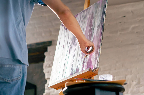 ブルーTシャツのアーティストがパレットナイフでキャンバスに描くアートワークで低撮影 - 写真・画像