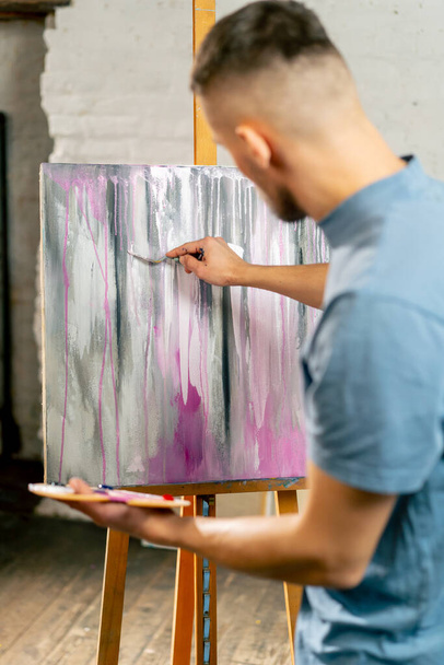 egy művészeti stúdióban egy művész összekeveri a színeket egy palettán, ami a kezében tartja - Fotó, kép
