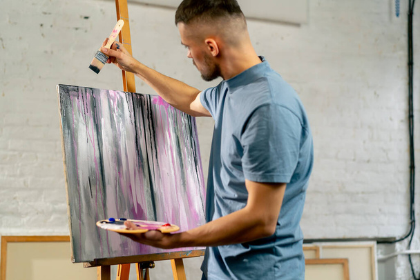 in an art studio the artist creates dark streaks on the canvas with a large brush - Photo, Image
