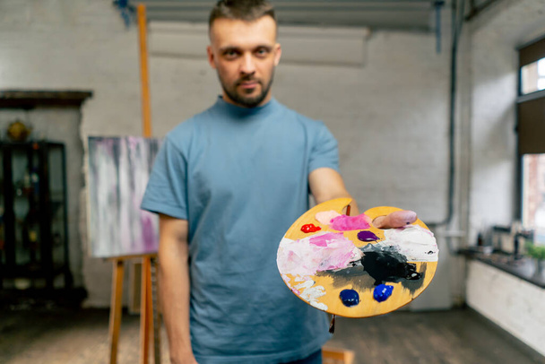 Bir sanat stüdyosunda bir sanatçı doğrudan kameraya bakar ve bir palet gösterir. - Fotoğraf, Görsel