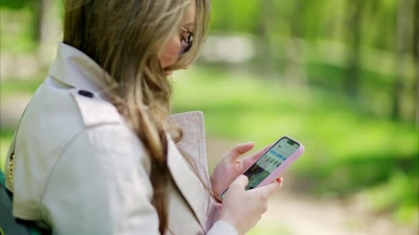 Vrouw scrollend door haar telefoon op een bankje in het park - Video