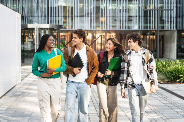 Mutlu öğrenci arkadaşlar üniversite kampüsünde yürüyor, dersten sonra sohbet ediyor ve dışarıda gülüyorlar. - Fotoğraf, Görsel