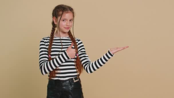Criança pré-adolescente menina mostrando polegares para cima apontando lugar vazio direito, área de publicidade para texto de desconto comercial, espaço de cópia para propaganda de promoção de mercadorias. Crianças adolescentes em fundo bege - Filmagem, Vídeo